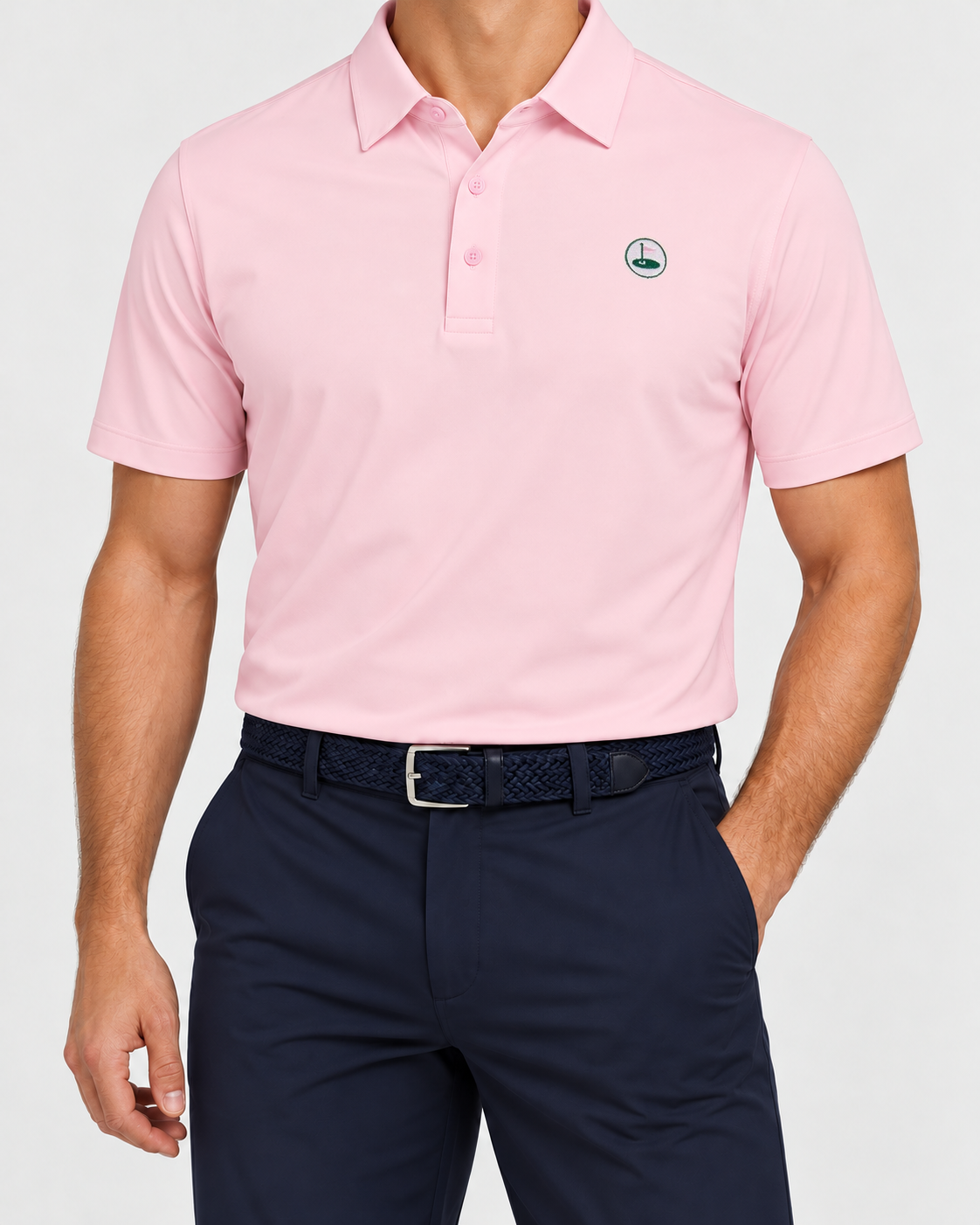 Palvento Brancaster pink performance polo with an embroidered chest roundel, worn with navy golf trousers and a navy woven belt.