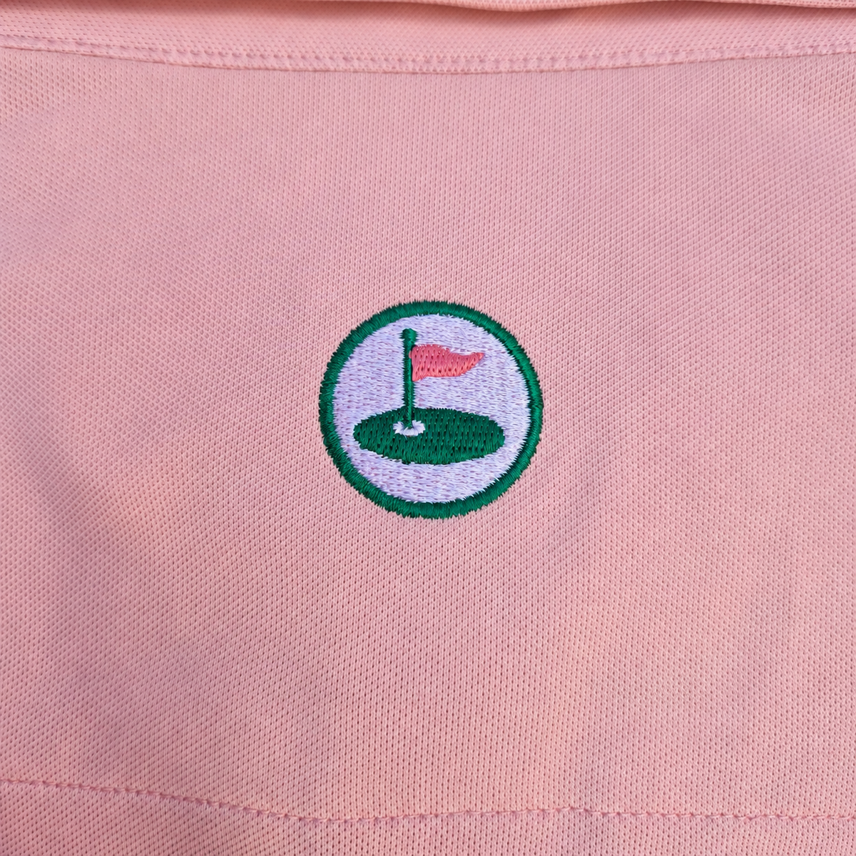 Close-up of the Palvento Golf signature pink roundel logo, a distinctive detail of the independent British golfwear brand.